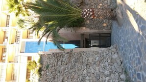 Ein Steinweg führt zu einem Hauseingang, mit einer Palme und einer dekorativen Ananas-Skulptur.