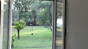A view through a glass door into a yard with a lawn, a tree, and a hanging object. - VILLA IL CARRUBO-unit2 € 500 per week with 3 bedrooms for 10 persons (Pisticci)