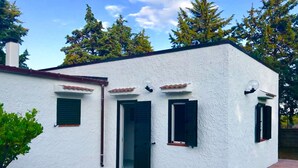 A white building with three windows and a door, surrounded by a small garden and trees. - VILLA IL CARRUBO-unit2 € 500 per week with 3 bedrooms for 10 persons (Pisticci)