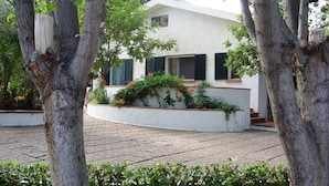A white building with black shutters, surrounded by trees and greenery. - VILLA IL CARRUBO-unit2 € 500 per week with 3 bedrooms for 10 persons (Pisticci)
