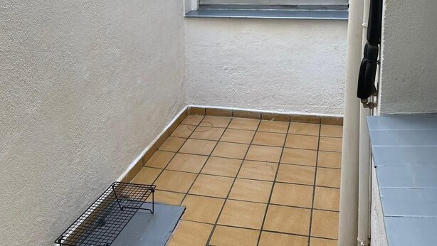 Un petit balcon fermé, doté d’un sol carrelé, d’une étagère en métal et d’une fenêtre munie d’un moustiquaire.
