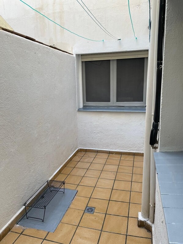 A small, enclosed balcony with a tiled floor, a metal shelf, and a window with a screen. - Cozy apartment near the beach (Carboneras)