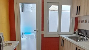 Une cuisine avec un mur rouge, une porte blanche et une fenêtre.
