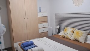 Une chambre à coucher comprenant un lit, une armoire, une table de chevet, une lampe et un ventilateur de plafond.