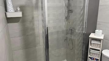 Een moderne badkamer met een douchecabine, toilet en een plank met toiletartikelen.