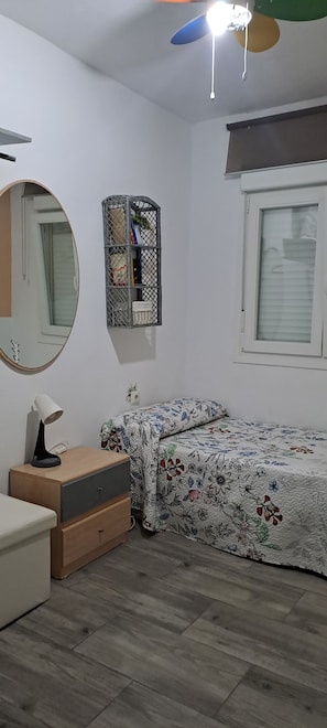 Ein Schlafzimmer mit einem Bett, einem Nachttisch, einem Spiegel, einem Kleiderschrank und einem Deckenventilator.