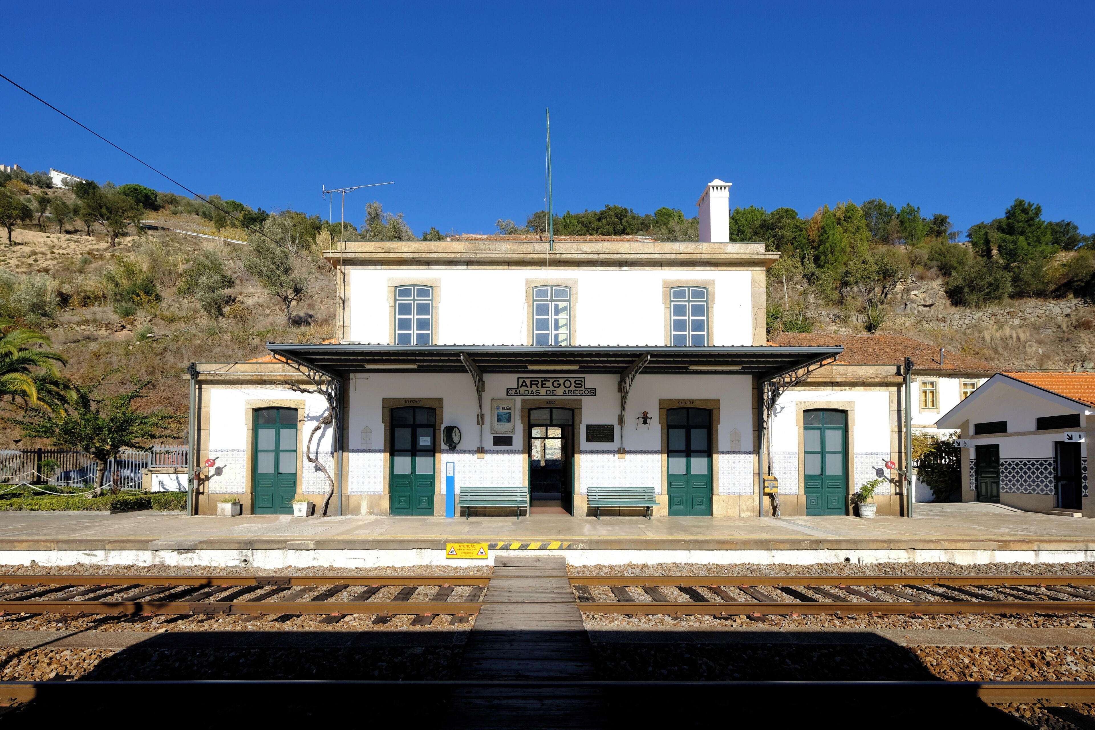 Una estación de tren con un edificio blanco, puertas verdes y un reloj.