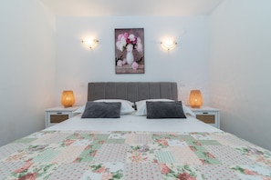 A bedroom with a bed, two bedside lamps, a floral painting on the wall, and a quilt on the bed. - SABLIC 3 apartment with sea view, 30m from a beach in OKRUG GORNJI (Okrug Gornji)