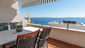 A terrace with a table and chairs, a striped awning, and a view of the sea. - SABLIC 3 apartment with sea view, 30m from a beach in OKRUG GORNJI (Okrug Gornji)
