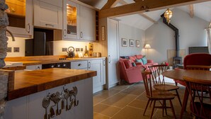 A kitchen with wooden beams, a dining area with a red sofa, and a stone wall.