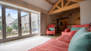 A spacious living room with a large sliding glass door leading to a garden, a stone fireplace, and a cozy seating area with pink sofas.