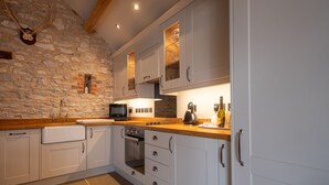 A kitchen with white cabinets, a stone wall, a wooden countertop, a sink, a microwave, and a kettle.