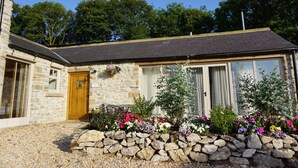 A stone house with a wooden door, large windows, and a gravel driveway.