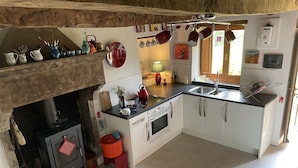 Une cuisine de taille réduite avec des meubles blancs, une cuisinière et un évier. On peut voir des casseroles suspendues et une bouilloire rouge accrochée au mur.