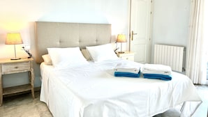 A neatly made bed with white linens and two folded towels, a bedside table with a lamp, a radiator, and a door with a handle. - House with spectacular sea views in the historic centre of Begur (Begur)