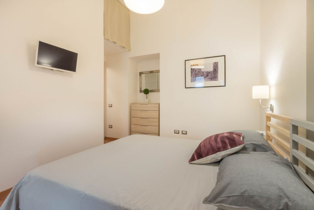 Una camera da letto con un letto, una televisione a muro, un comò e un quadro incorniciato.