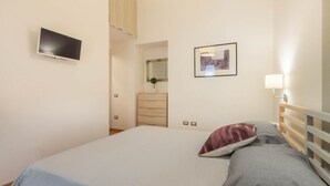 Een slaapkamer met een bed, een aan de muur bevestigde televisie, een dressoir en een ingelijste foto.