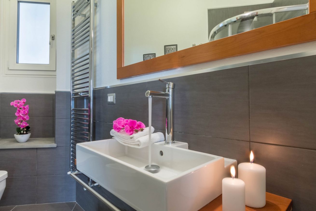 Un bagno moderno con un lavandino bianco, un portascopevoli e uno specchio sopra il lavandino.