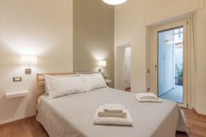 A hotel room with a bed, bedside lamps, a small bedside table, and a view of the outside through a glass door.