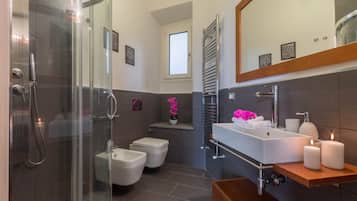 Un bagno moderno con cabina doccia in vetro, lavabo bianco con mobile contenitore in legno e un grande specchio sopra il lavabo.