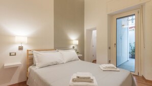 A hotel room with a bed, bedside lamps, a small bedside table, and a view of the outside through a glass door. - HELMI34 - A flat with all comforts in the centre of Cagliari (Cagliari)