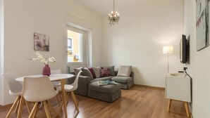 A modern living room with a dining area, a grey sofa set, a chandelier, and a flat-screen TV mounted on the wall. - HELMI34 - A flat with all comforts in the centre of Cagliari (Cagliari)