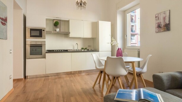 A modern kitchen with white cabinets, a microwave, and an oven. There is a dining area with a white table and chairs, and a book on a couch. - HELMI34 - A flat with all comforts in the centre of Cagliari (Cagliari)