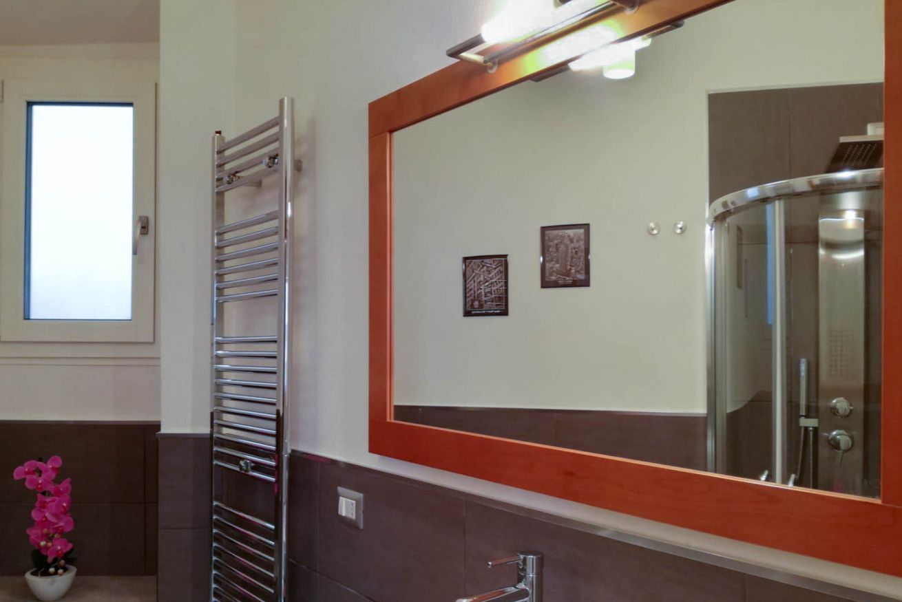 Un bagno con box doccia in vetro, portasciugamani e uno specchio con cornice in legno.