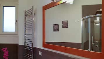 Un bagno con box doccia in vetro, portasciugamani e uno specchio con cornice in legno.