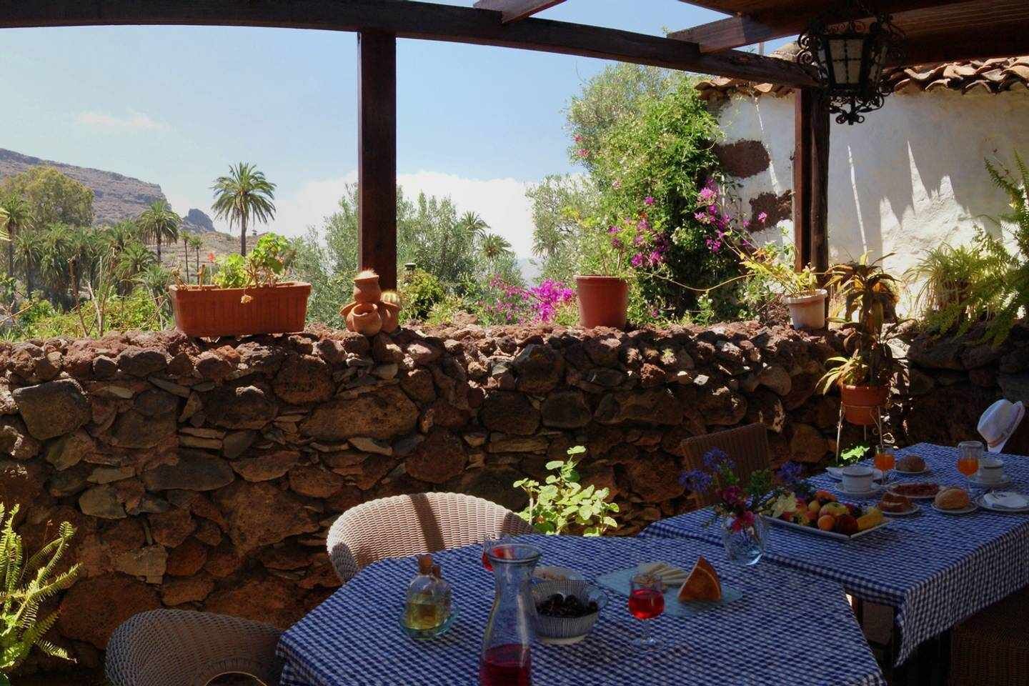 Un área de comedor al aire libre con paredes de piedra, plantas en macetas y una mesa lista para una comida.