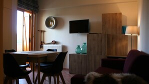 A compact living space with a dining area, a TV mounted on the wall, and a sofa.
