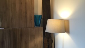 A room with a wooden cabinet, a blue glass vase, a pair of skis leaning against the wall, and a lamp with a white shade.