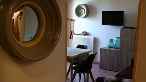 A hallway leading to a dining area with a round mirror, a table, chairs, and a television mounted on the wall.