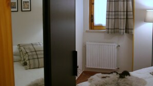 A bedroom with a bed, a window with a plaid curtain, a radiator, and a wooden door.