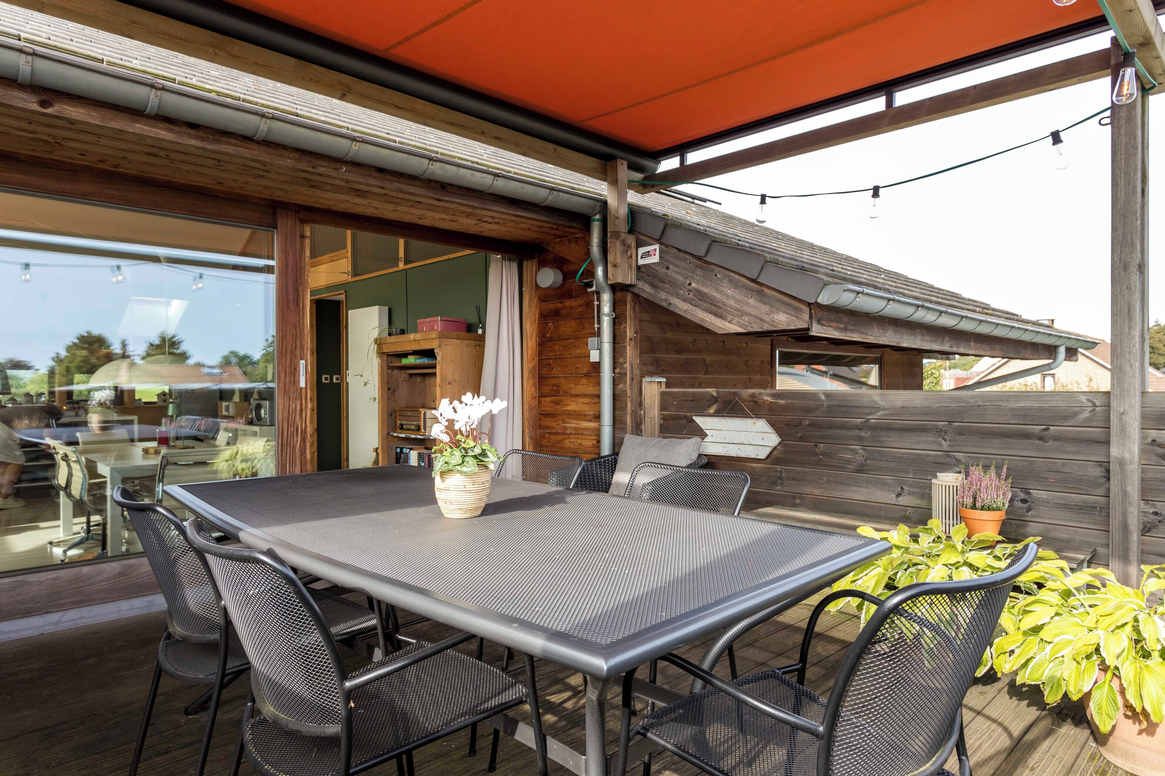 An outdoor patio with a metal table and chairs, surrounded by potted plants and a wooden fence.