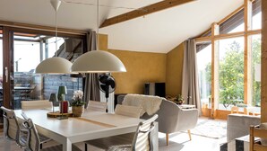 A modern dining area with a white table, metal chairs, and a large window with curtains. - StroEnzo - Cozy straw-bale holiday home - Tongeren / Maastricht - 5pers   (Riemst)