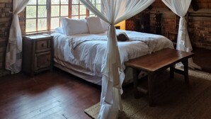 Une chambre avec un lit sous un dais, des poutres en bois au plafond et un mur en briques.
