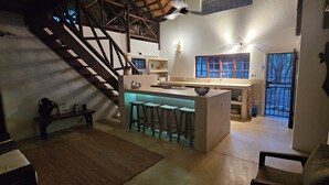 Une cuisine spacieuse dotée d’un îlot central, de tabourets de bar en bois, d’un escalier et offrant une vue sur l’extérieur grâce à de grandes fenêtres.