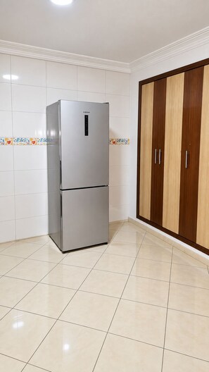 A kitchen with a stainless steel refrigerator, white tiled walls, and a wooden wardrobe.