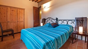Een slaapkamer met een bed, een houten garderobe en een nachtkastje met een lamp.