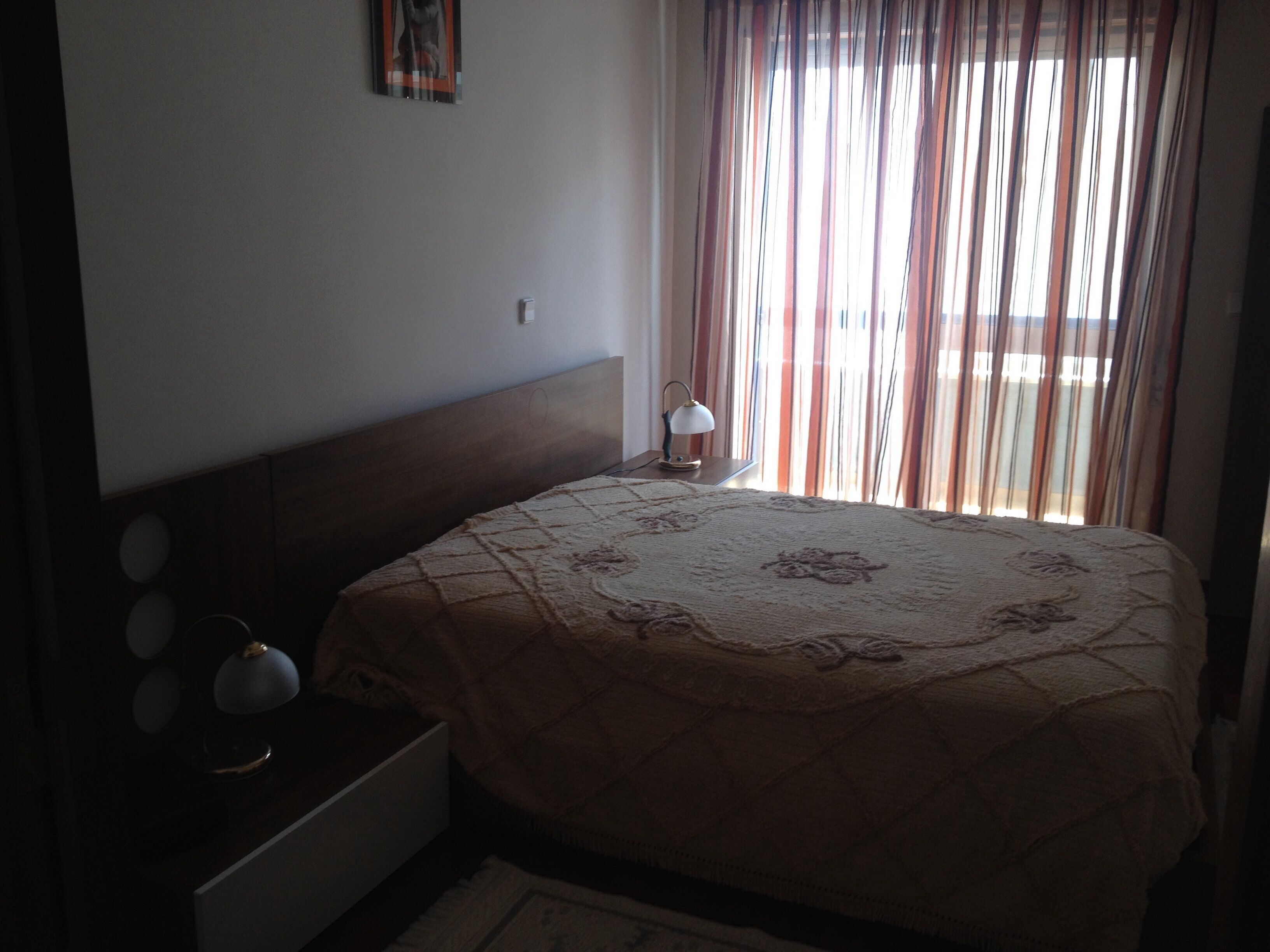 A bedroom with a bed, a nightstand, a lamp, and a window with curtains.