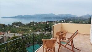 En balkon med fletstole med udsigt over et kystlandskab med bjerge i det fjerne.