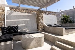 A modern outdoor seating area with stone walls, a pergola, and a potted plant. - Design Suite Γ, with Sea view, Shared pool , Pool bar, Gym (Mykonos)