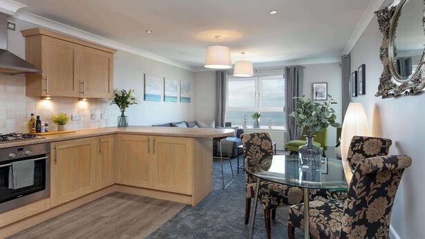Una cocina moderna con armarios de madera, una isla central y un comedor con sillas estampadas y una mesa de vidrio.