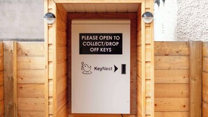 Una caja de madera KeyNest con un letrero que indica abrir para recogida o devolución de llaves.