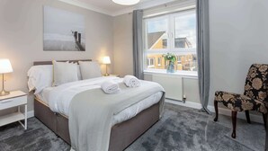 Habitación de hotel ordenada con cama, lámparas de noche, una silla y ventana con vistas a edificios.