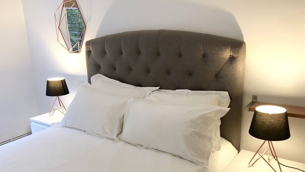 Una cama bien hecha con sábanas blancas, un cabecero capitonado y dos lámparas de noche con pantallas negras.