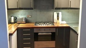 Una cocina compacta con gabinetes oscuros, una estufa a gas, horno integrado y salpicadero de azulejos.