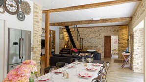 A dining area with a long table set for six, a refrigerator, and a staircase leading to an upper level.