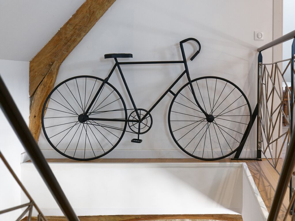 A black bicycle hanging from a wooden beam in a room with white walls and a wooden floor.